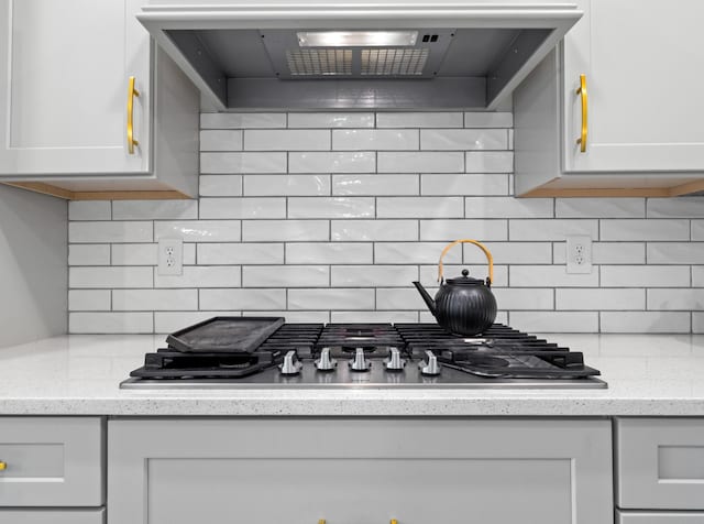 kitchen featuring stainless steel gas cooktop, wall chimney range hood, white cabinetry, and decorative backsplash