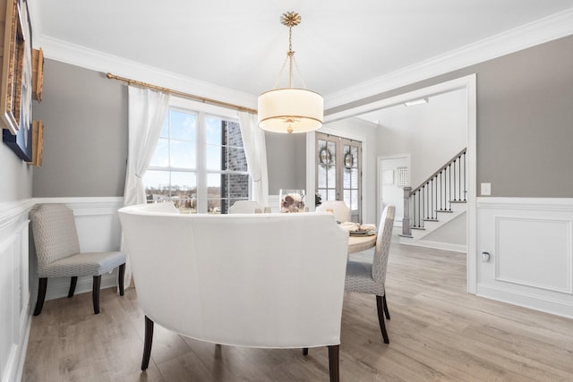 dining space featuring ornamental molding, a wainscoted wall, light wood-style floors, and stairway