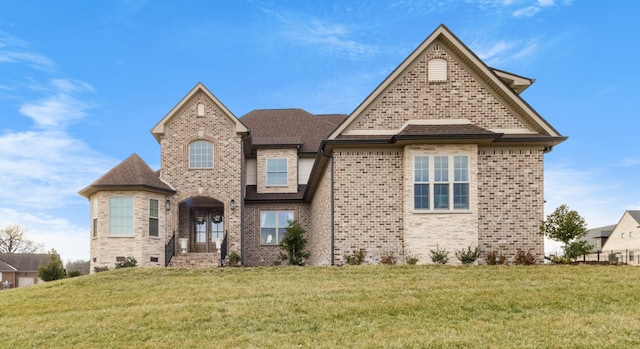 view of front of house with roof with shingles, a front yard, and brick siding