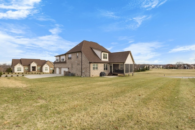 rear view of house with a garage, concrete driveway, a sunroom, a yard, and brick siding