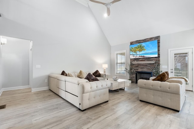 living area featuring high vaulted ceiling, light wood-type flooring, a stone fireplace, and baseboards