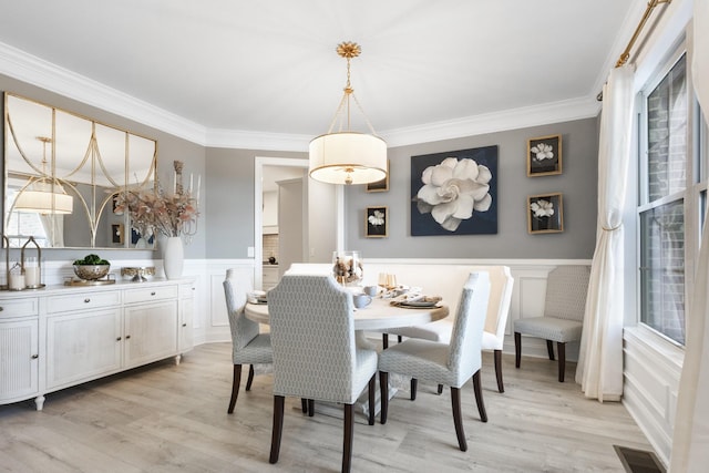 dining room featuring light wood-style floors, wainscoting, visible vents, and crown molding