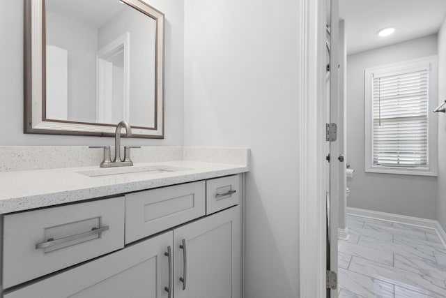 bathroom featuring toilet, marble finish floor, vanity, and baseboards