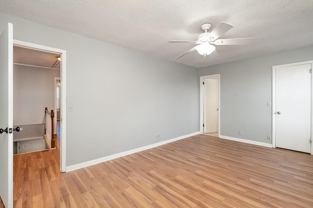 unfurnished bedroom featuring light wood finished floors, attic access, baseboards, and a textured ceiling