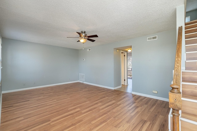 unfurnished room featuring ceiling fan, visible vents, baseboards, stairs, and light wood finished floors