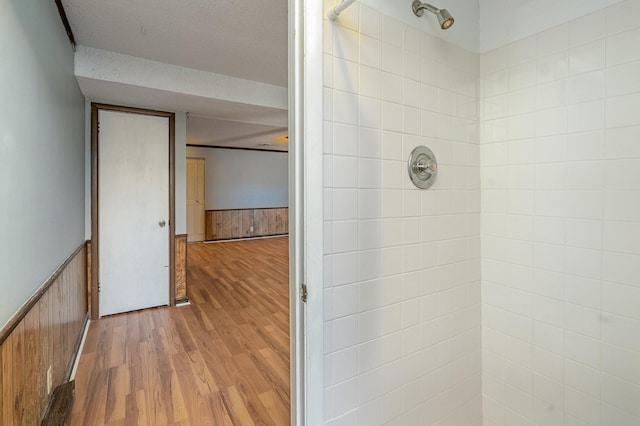 full bath featuring a wainscoted wall, a tile shower, a textured ceiling, and wood finished floors