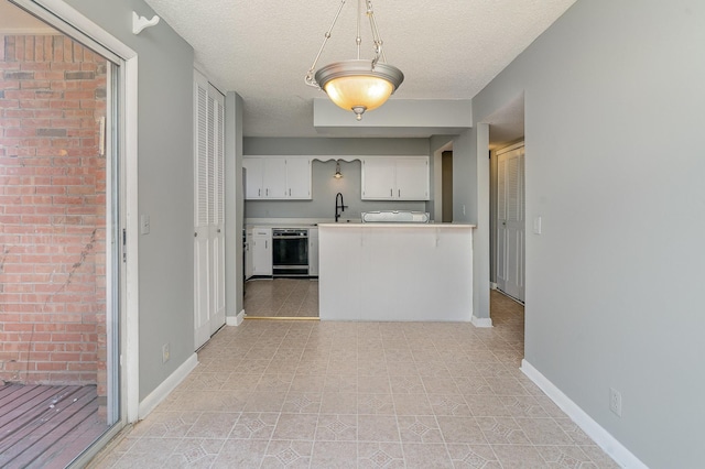 kitchen featuring baseboards, white cabinets, dishwasher, light countertops, and a textured ceiling