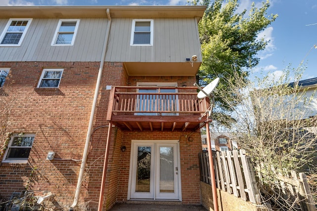 rear view of property with brick siding, fence, and a balcony