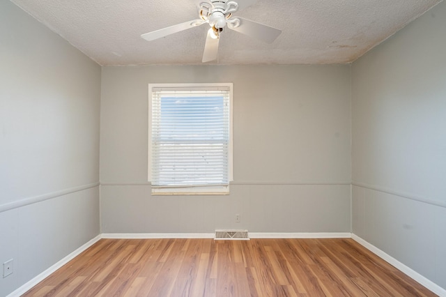 spare room featuring a ceiling fan, visible vents, a textured ceiling, and wood finished floors