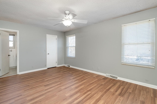 unfurnished room with baseboards, light wood-style flooring, visible vents, and a textured ceiling