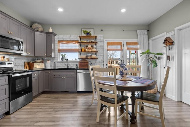 kitchen featuring tasteful backsplash, appliances with stainless steel finishes, gray cabinets, light wood-style floors, and a sink