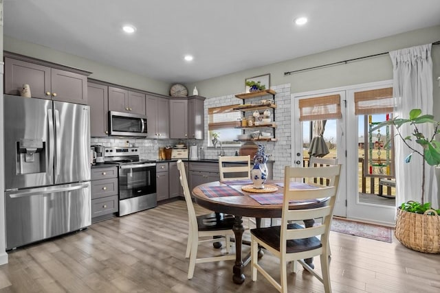 kitchen with dark countertops, stainless steel appliances, gray cabinetry, light wood-style floors, and backsplash