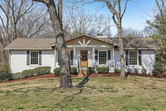 view of front facade featuring a porch, brick siding, a shingled roof, and a front lawn