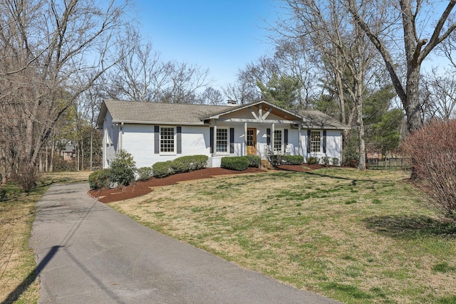 view of front of property featuring aphalt driveway, brick siding, fence, a front lawn, and a chimney