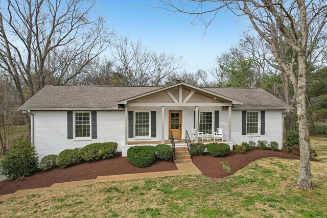 view of front of home featuring brick siding, a front yard, a porch, and a shingled roof