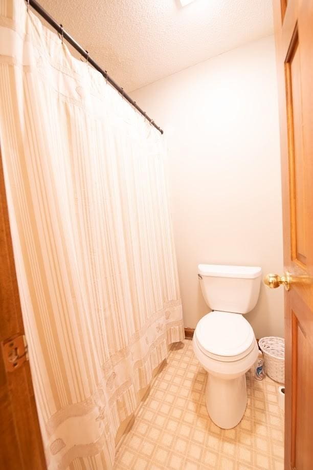 full bath with curtained shower, a textured ceiling, toilet, and tile patterned floors