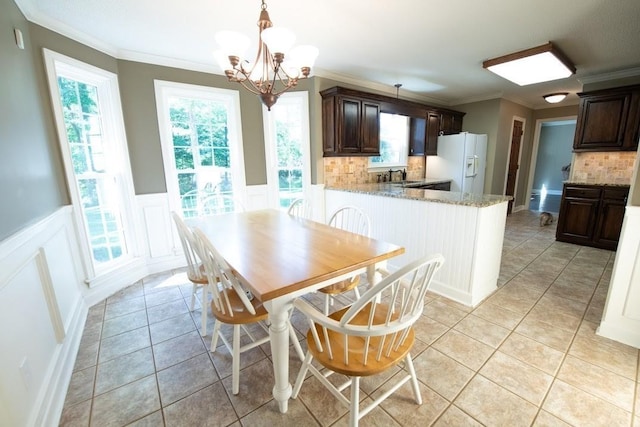 dining area featuring light tile patterned floors, a notable chandelier, crown molding, and a wainscoted wall