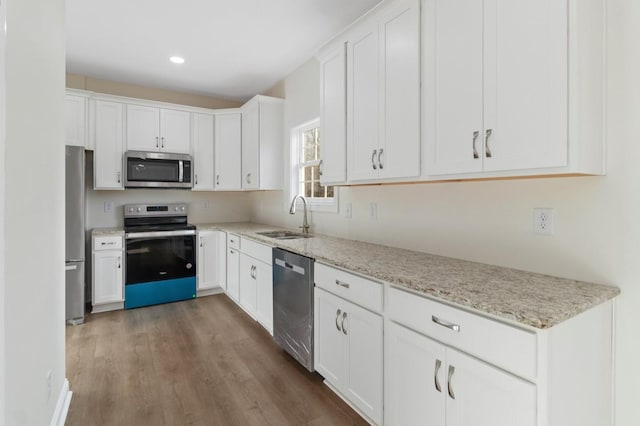 kitchen with white cabinets, wood finished floors, light stone countertops, stainless steel appliances, and a sink