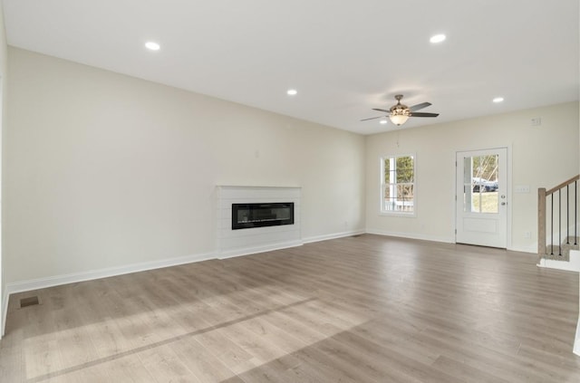 unfurnished living room with recessed lighting, stairway, wood finished floors, and a glass covered fireplace