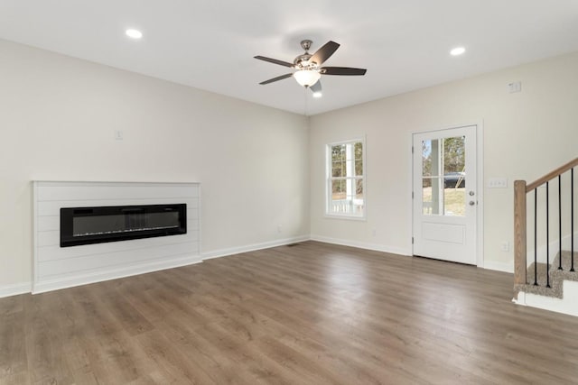 unfurnished living room featuring ceiling fan, wood finished floors, baseboards, stairs, and a glass covered fireplace