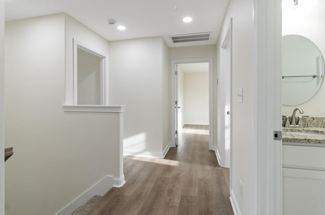 corridor with baseboards, visible vents, wood finished floors, a sink, and recessed lighting