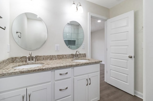 full bath with double vanity, baseboards, a sink, and wood finished floors