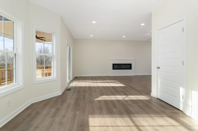 unfurnished living room with baseboards, wood finished floors, a glass covered fireplace, and recessed lighting