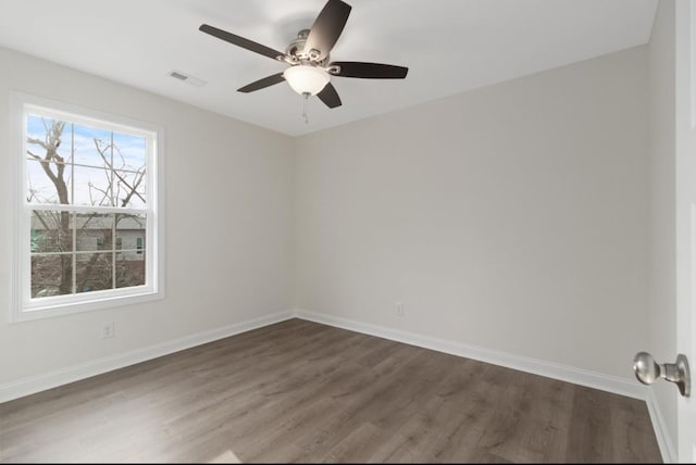 empty room with dark wood-style flooring, visible vents, and baseboards