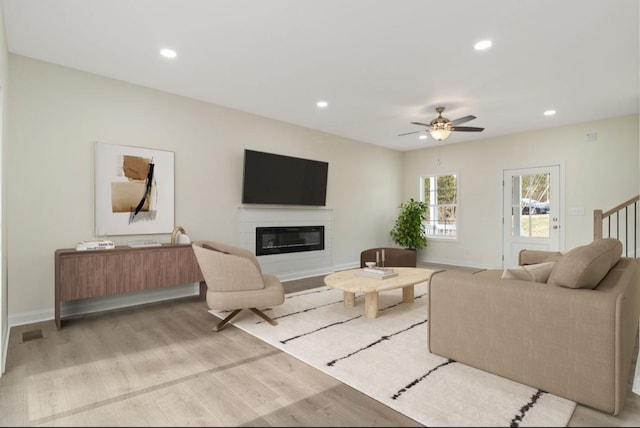 living room with recessed lighting, light wood-style flooring, baseboards, and a glass covered fireplace