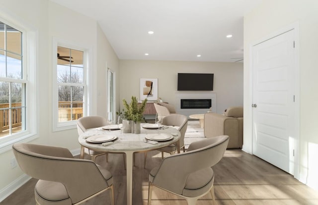 dining space with light wood-style floors, a glass covered fireplace, baseboards, and recessed lighting