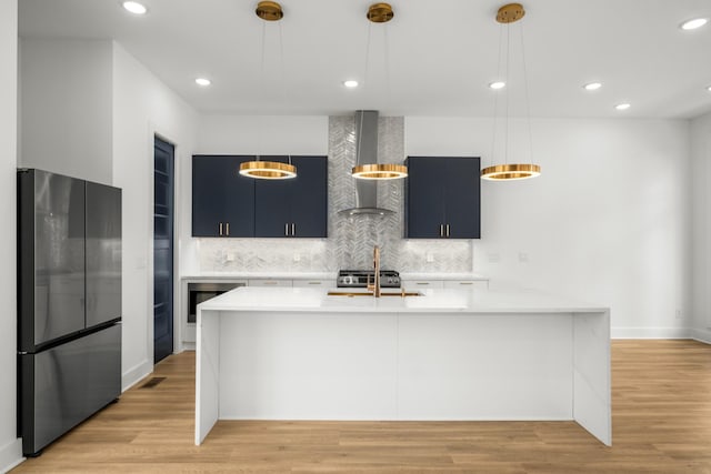 kitchen featuring light countertops, freestanding refrigerator, decorative backsplash, wall chimney exhaust hood, and light wood finished floors