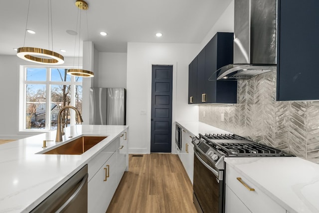 kitchen with stainless steel appliances, decorative backsplash, a sink, wall chimney range hood, and dark cabinetry