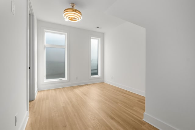 empty room featuring light wood finished floors, visible vents, and baseboards