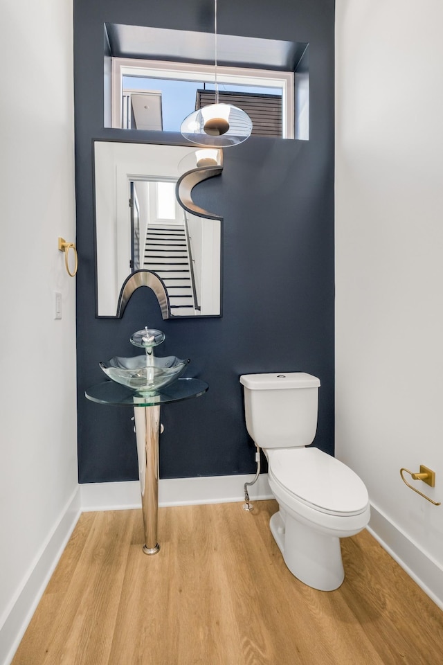 half bath with wood finished floors, toilet, and baseboards