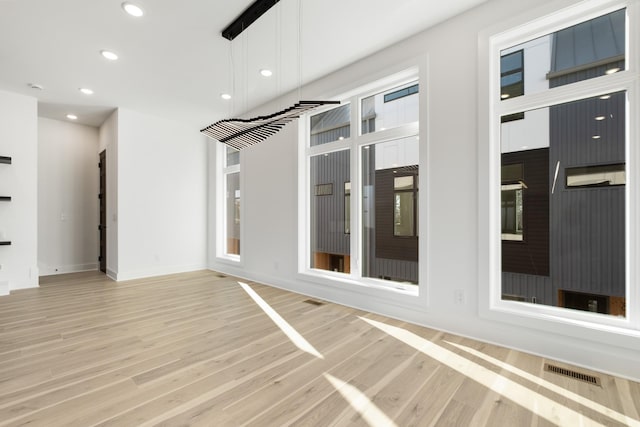 empty room featuring light wood finished floors, a wealth of natural light, recessed lighting, visible vents, and baseboards