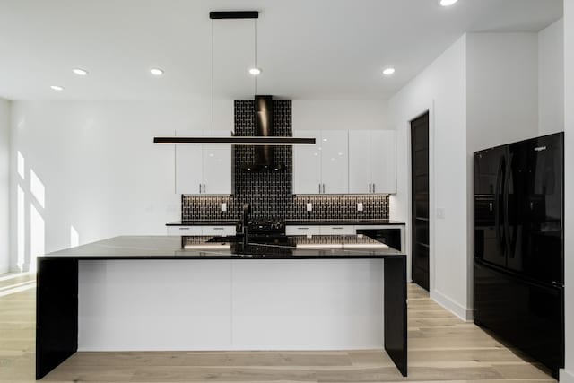 kitchen with light wood-type flooring, black fridge, dark countertops, and white cabinetry