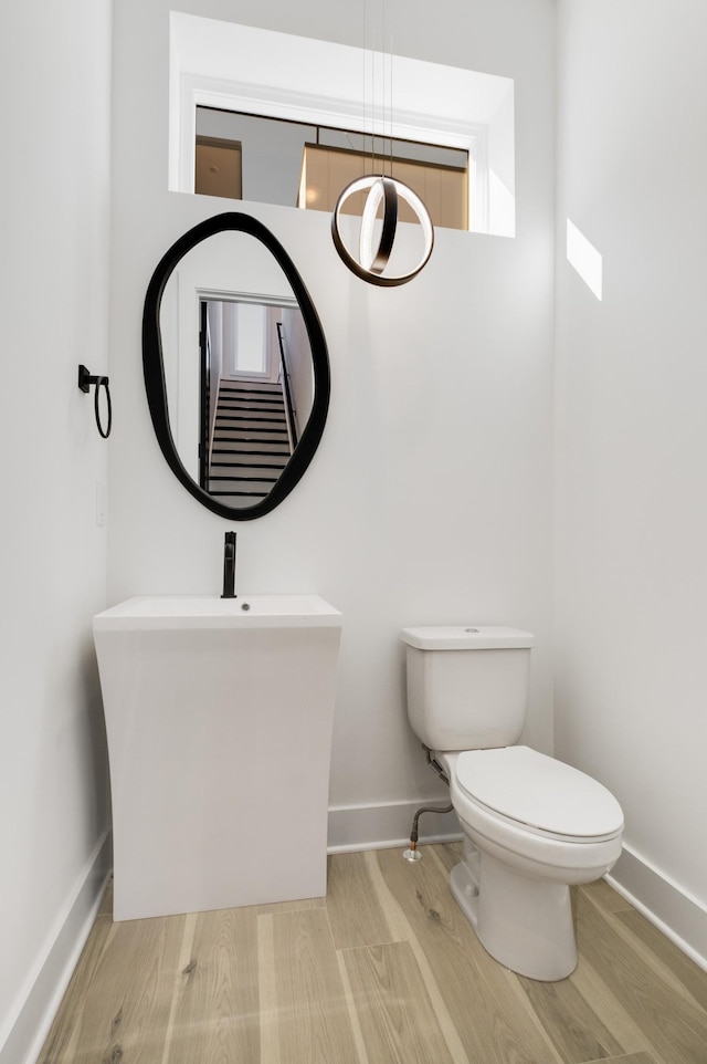 half bathroom with baseboards, toilet, and wood finished floors