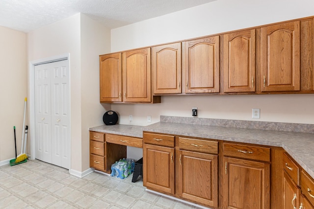 kitchen featuring brown cabinets, light floors, built in study area, a textured ceiling, and baseboards