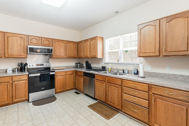 kitchen featuring light floors, appliances with stainless steel finishes, a sink, and brown cabinets