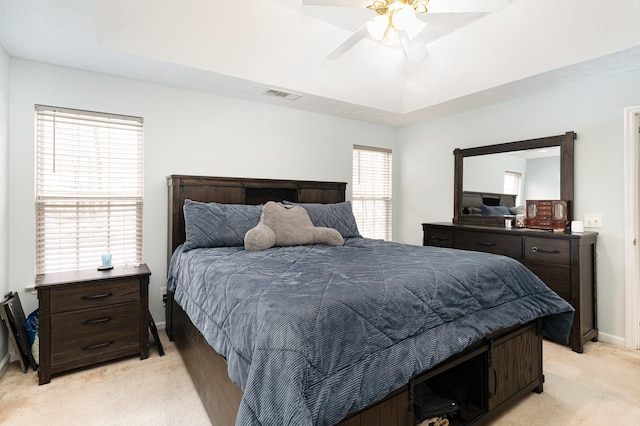 bedroom with a raised ceiling, visible vents, ceiling fan, and light carpet