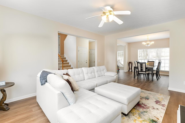 living room featuring ceiling fan with notable chandelier, stairway, wood finished floors, and baseboards