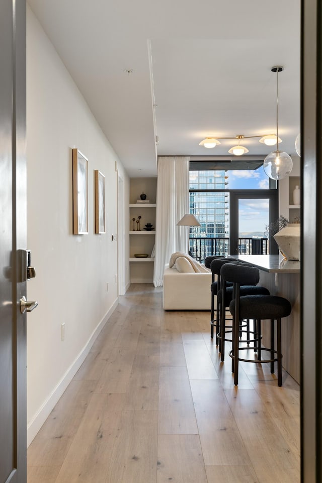 corridor featuring baseboards, built in shelves, and light wood finished floors