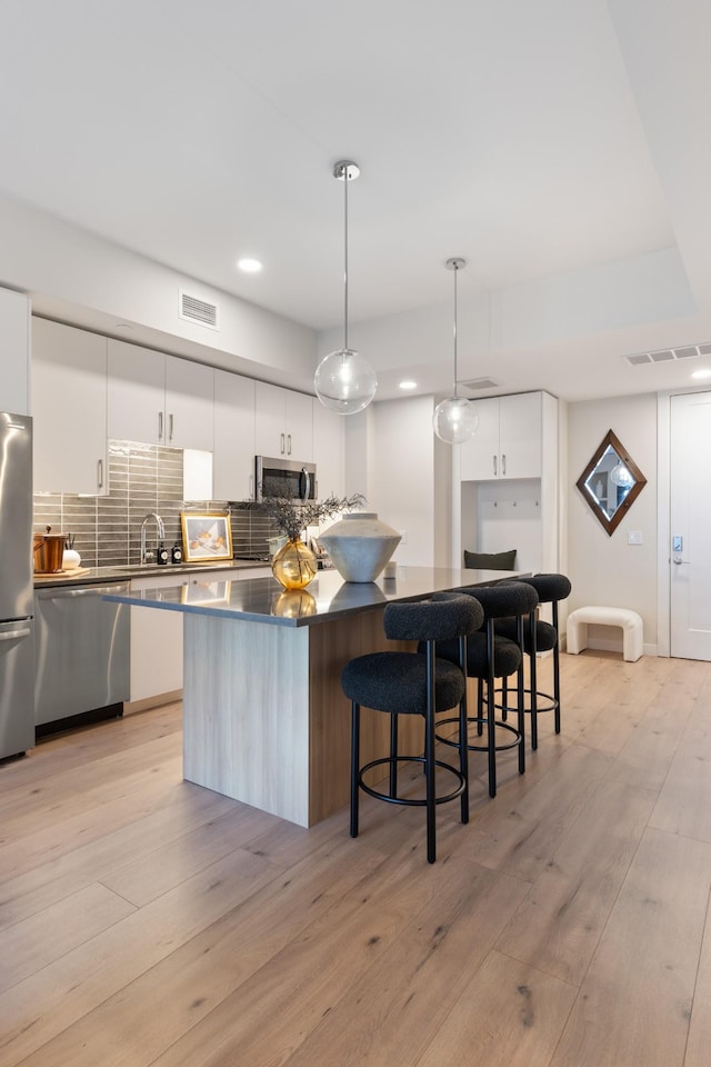 kitchen with light wood-type flooring, visible vents, modern cabinets, appliances with stainless steel finishes, and decorative backsplash