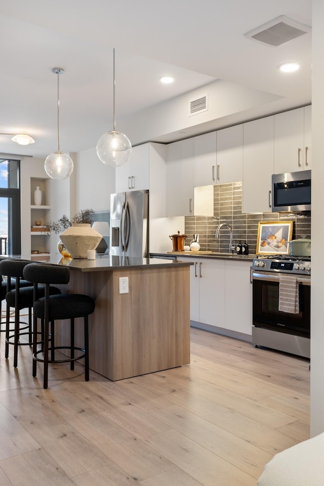 kitchen with dark countertops, a kitchen breakfast bar, visible vents, and stainless steel appliances