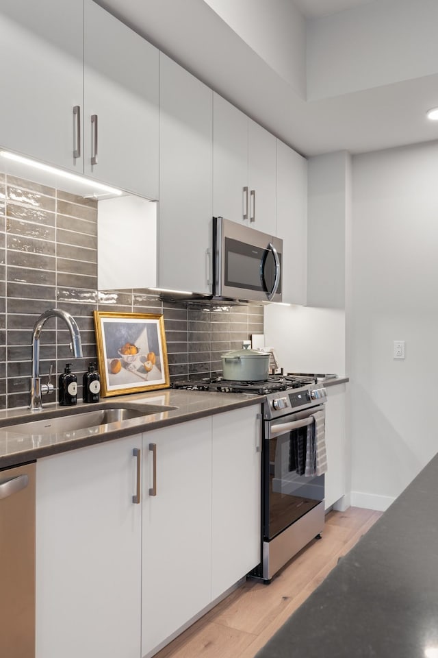 kitchen with a sink, stainless steel appliances, white cabinets, tasteful backsplash, and light wood-type flooring