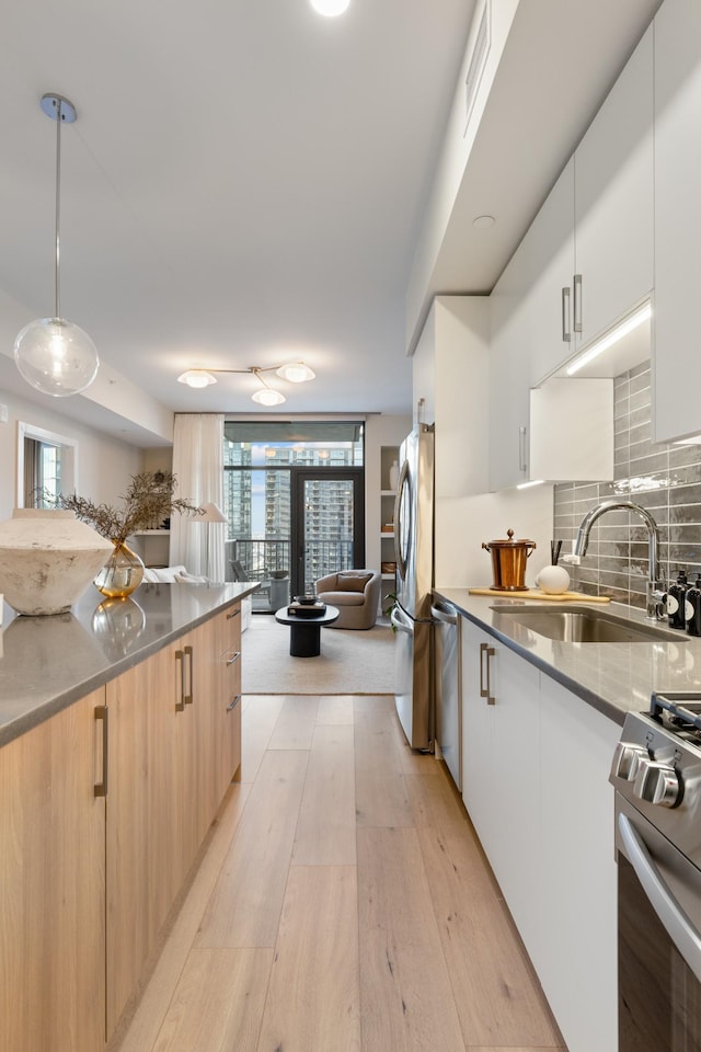 kitchen with light wood-style flooring, a sink, appliances with stainless steel finishes, modern cabinets, and backsplash