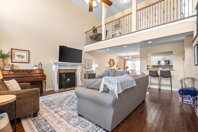 living area featuring dark wood-type flooring, a lit fireplace, baseboards, and ceiling fan with notable chandelier