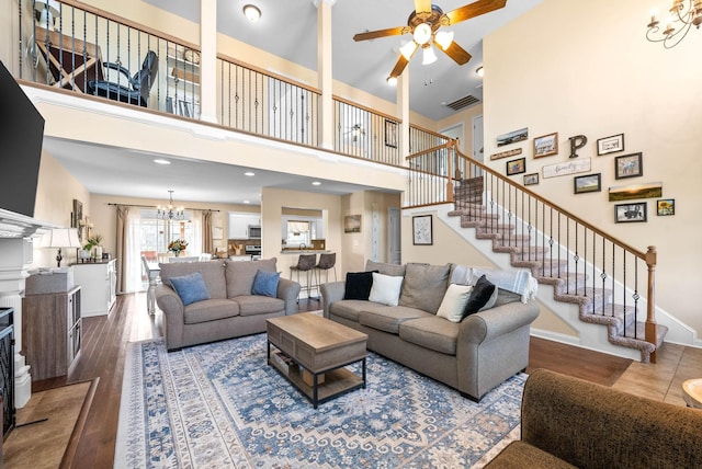 living room with visible vents, stairway, wood finished floors, baseboards, and ceiling fan with notable chandelier