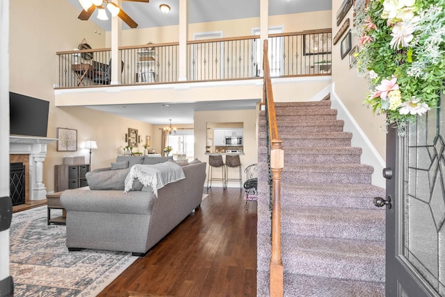 living area with a towering ceiling, stairway, hardwood / wood-style floors, a fireplace, and ceiling fan with notable chandelier