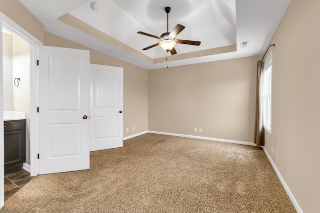 interior space with baseboards, a raised ceiling, connected bathroom, ceiling fan, and carpet flooring